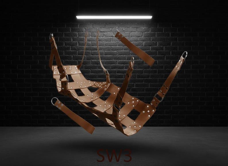 A brown leather sling with a woven design, metal rings and straps. The product is suspended in the air against a dark brick wall background. The letters "SW3" are visible at the bottom.