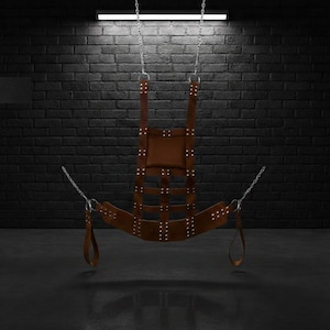 A brown leather swing suspended by silver chains. The swing has a padded seat and backrest, with multiple straps and rivets. The text "SW1 BRW" is visible at the bottom.