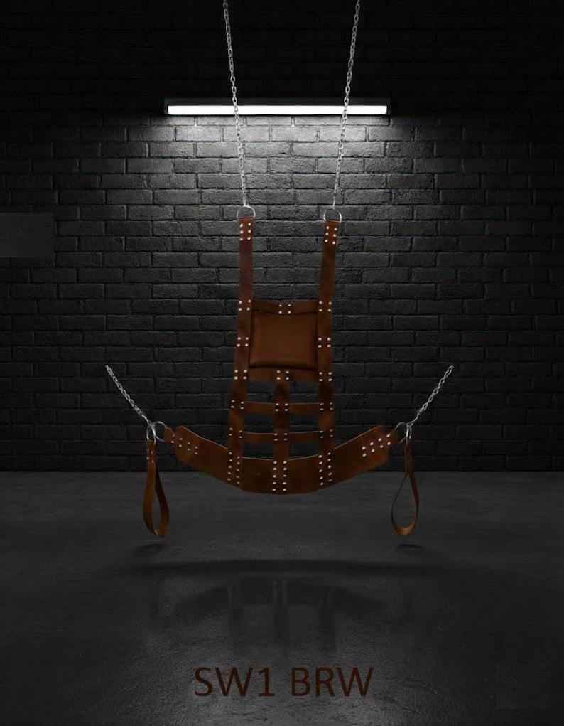 A brown leather swing suspended by silver chains. The swing has a padded seat and backrest, with multiple straps and rivets. The text "SW1 BRW" is visible at the bottom.