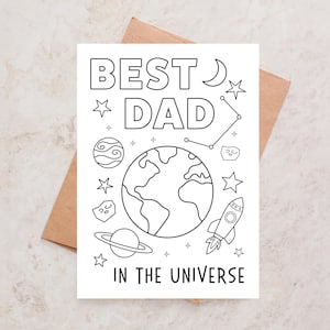 Puede incluir: Una tarjeta de felicitación rectangular blanca con dibujos de líneas negras de elementos espaciales que incluyen un planeta, un cohete, estrellas, una luna creciente y el texto BEST DAD IN THE UNIVERSE, sobre un sobre de papel marrón.