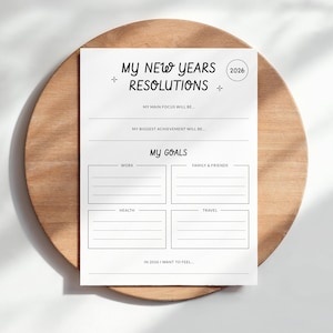 May include: A white paper with the text "MY NEW YEARS RESOLUTIONS" and "2026" in a circle. Below are sections for goals, including "WORK", "FAMILY & FRIENDS", "HEALTH", and "TRAVEL". The paper is on a wooden surface.