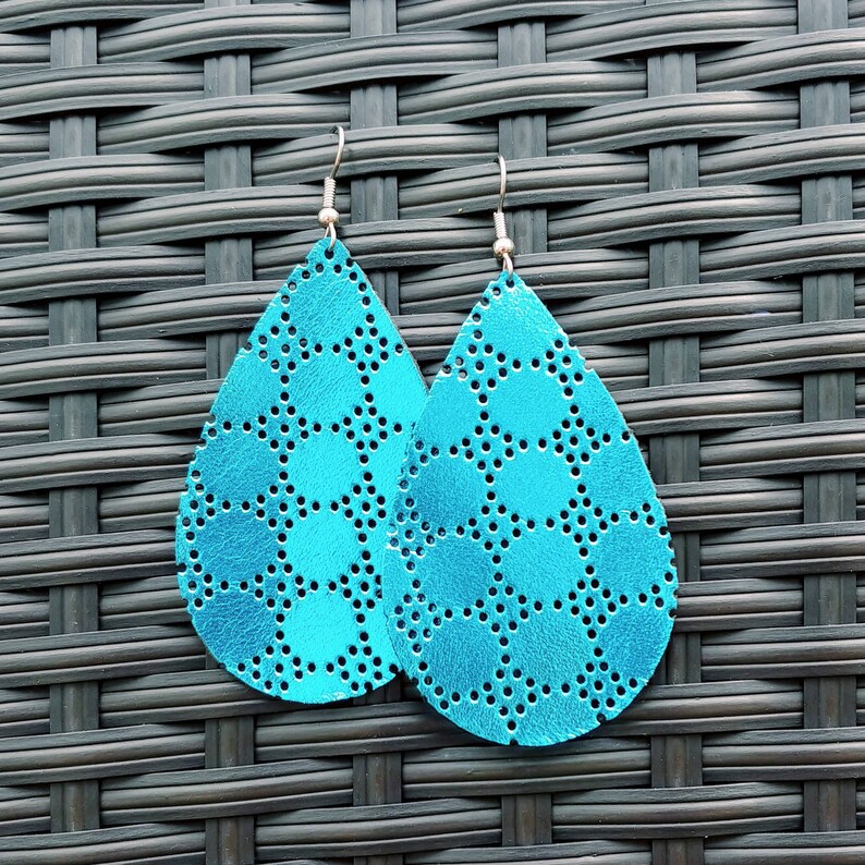 May include: A pair of turquoise blue teardrop-shaped earrings with a geometric pattern. The earrings are made of leather and have a metallic finish.