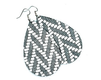 May include: A pair of teardrop-shaped earrings with a black and white geometric pattern. The earrings are made of leather and have silver hooks.