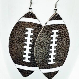 May include: A pair of brown leather earrings shaped like footballs with white stitching. The earrings have silver hooks.