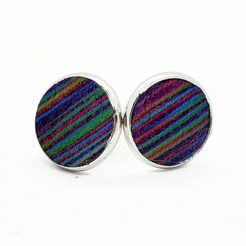 May include: A pair of silver stud earrings with a round, colorful fabric design. The fabric has a striped pattern in shades of purple, green, red, and blue.