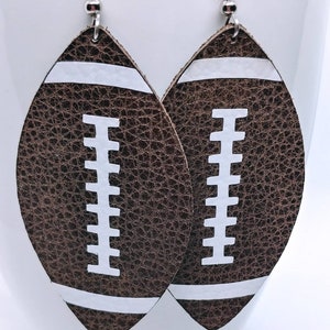 May include: A pair of brown leather earrings shaped like footballs with white stitching and white stripes.
