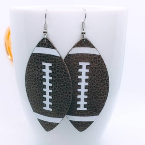 May include: A pair of brown leather earrings shaped like footballs with white stitching and white stripes.