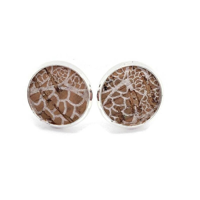 May include: A pair of silver stud earrings with a round cork base featuring a white lace pattern.