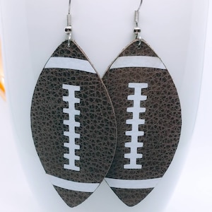 May include: A pair of brown leather earrings shaped like footballs with white stitching and white stripes.