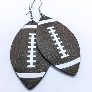 May include: A pair of brown leather earrings shaped like footballs with white stitching and white stripes.