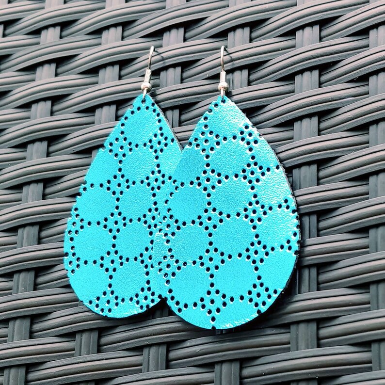 May include: A pair of turquoise blue teardrop-shaped earrings with a geometric pattern. The earrings are made of leather and have a silver-toned hook closure.