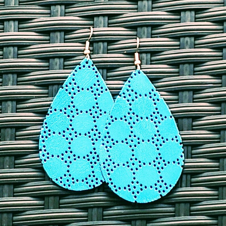 May include: A pair of turquoise blue teardrop-shaped earrings with a geometric pattern. The earrings are made of leather and have gold-colored hooks.