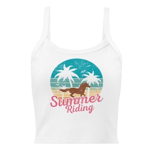 May include: White crop top with a graphic featuring a brown horse running in front of a sunset with palm trees and the words "Summer Riding" in pink and red. The top has thin straps.