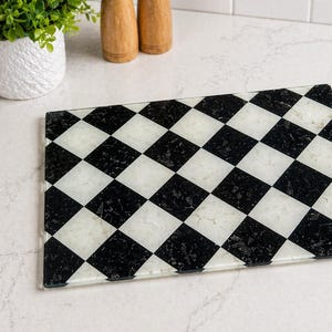 Rectangular glass cutting board with a black and white checkerboard pattern. The board is made of clear glass and has a decorative design. Kitchen and dining decor.