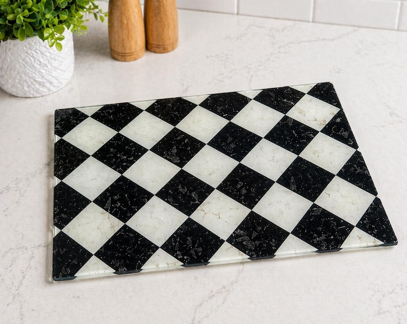 Rectangular glass cutting board with a black and white checkerboard pattern. The board is made of clear glass and has a decorative design. Kitchen and dining decor.