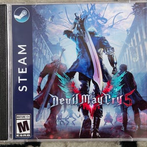May include: A video game case for "Devil May Cry 5" featuring a dynamic action scene with multiple characters and a large sword. The case includes the Steam logo and ESRB rating.