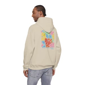 Pode incluir: Moletom bege com um design floral colorido nas costas. O design apresenta flores em vermelho, amarelo, azul e rosa. O moletom tem capuz e um ajuste relaxado, adequado para uso casual.