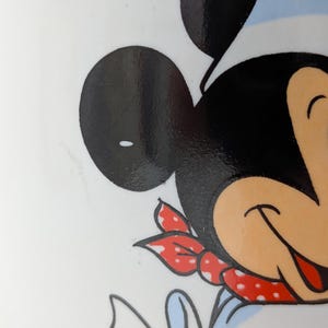 May include: Close-up of a cartoon character's face, featuring large black ears, a chef's hat, and a red polka-dot neckerchief. The character's face is a light tan color, with a smiling expression. The background is white.