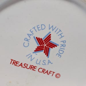 May include: Close-up of a white ceramic surface with a circular emblem. The emblem features a red and blue star design, surrounded by the text "CRAFTED WITH PRIDE IN U.S.A." and "TREASURE CRAFT" in red and blue lettering.
