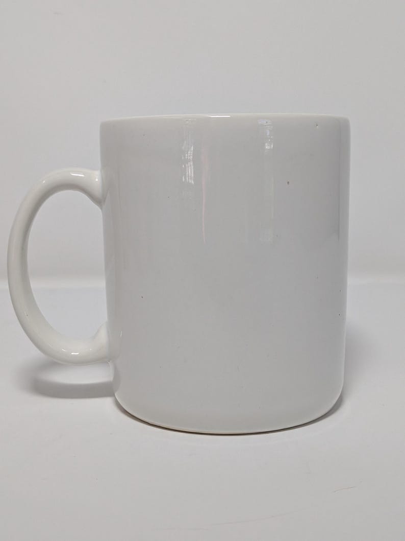 May include: A white ceramic mug with a curved handle. The mug has a cylindrical shape and a smooth, glossy finish. The mug is empty and sits on a white surface.