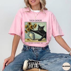 May include: Pink t-shirt featuring a framed image of a black cat reaching for sunflowers in a vase, a parody of Van Gogh's artwork. The text "VAN GOGH" and "SUNFLOWERS (THIRD VERSION) - 1888" are printed above and below the image.