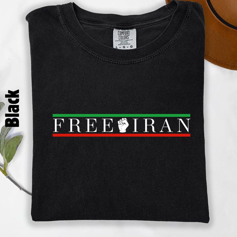 May include: Black t-shirt with the text "FREE IRAN" in white, with a green and red stripe design. The shirt features a white fist graphic. The tag reads "Comfort Colors".