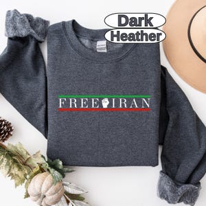 May include: Dark heather gray sweatshirt with the text "FREE IRAN" in green and white, with a red stripe. The sweatshirt has a crew neck and long sleeves. A tan hat is visible in the background.