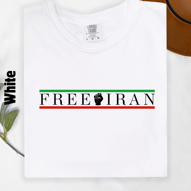 May include: White t-shirt with the text "FREE IRAN" in black, green, and red. The design includes a black fist graphic. The shirt is a Comfort Colors brand.