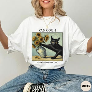 May include: White t-shirt featuring a graphic of a black cat reaching for sunflowers in a vase, inspired by Van Gogh's art. The text "VAN GOGH" is above the image, with "SUNFLOWERS (THIRD VERSION) - 1888" below.