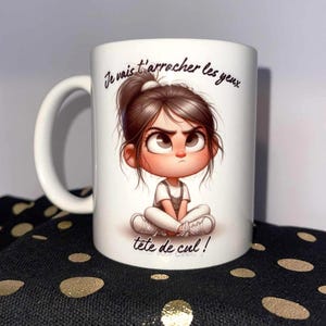 Peut inclure: Mug en céramique blanche avec une illustration d'une fille en colère et le texte "Je vais t'arracher les yeux tête de cul!". La fille porte une chemise blanche et une salopette. La tasse a une anse blanche.