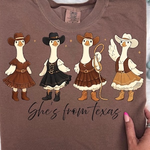 May include: A white ceramic mug with a black handle and the text "But First, Coffee" in a bold, black font. The mug is set against a blurred background, suggesting a cozy setting.