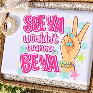 May include: White folded fabric with the text "SEE YA wouldn't wanna BE YA" in pink. A cartoon hand with blue fingernails makes a peace sign. The hand has a bracelet with yellow, pink, and blue beads. There are star and circle graphics.