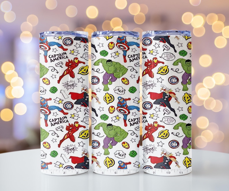 May include: Three white insulated tumblers featuring a repeating pattern of Marvel comic book characters. The design includes Captain America, Iron Man, Hulk, and Thor, with comic book speech bubbles and stars. The tumblers are approximately 25 cm tall.