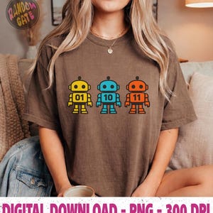 May include: A brown t-shirt featuring three colorful robot designs. The robots are yellow, blue, and orange, each with a different number: 01, 10, and 11. The text "DIGITAL DOWNLOAD - PNG - 300 DPI" is at the bottom.