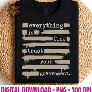 Puede incluir: Camiseta negra de cuello redondo con el texto "everything is fine trust your government" en blanco. El texto está superpuesto a pinceladas marrones. La camiseta se muestra sobre una superficie tejida beige.