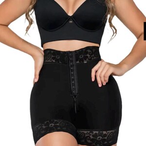 Könnte beinhalten: Schwarze Shapewear-Shorts mit hohem Bund, Reißverschluss und Hakenverschluss vorne. Die Shorts haben eine Spitzentrimmung an Taille und Beinöffnungen. Ein schwarzes BH-Oberteil ist ebenfalls sichtbar.