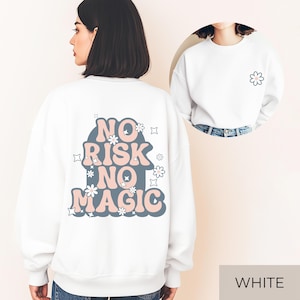 Könnte beinhalten: Weißes Sweatshirt mit dem Text "NO RISK NO MAGIC" in Rosa und Blau, mit Blumen- und Sterngrafiken. Ein kleineres Bild zeigt die Vorderseite des Sweatshirts mit einer Blumengrafik. Das Wort "WHITE" steht unten.