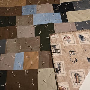 Può includere: Una trapunta patchwork con quadrati di denim e altri tessuti nei toni del marrone, beige, blu e verde. I quadrati sono cuciti insieme con filo bianco visibile. È visibile una seconda trapunta con immagini a tema pesca.