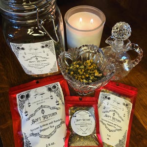 May include: An assortment of herbal tea products, including a glass jar, small red pouches, and a glass bowl. The pouches are labeled "Soft Return Nervous System and Anxiety Support Tea". A lit candle and a decorative glass bottle are also present.