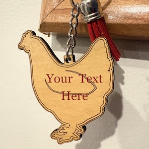 May include: A wooden chicken-shaped keychain with the text "Your Text Here" engraved in red. The keychain has a silver chain and a red tassel. The chicken is light brown with a detailed outline.
