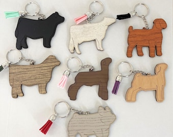 May include: Seven animal-shaped keychains made of wood and acrylic, featuring silhouettes of cattle, sheep, and a pig. Each keychain includes a metal ring and a small decorative tassel in colors including mint, pink, black, and purple.