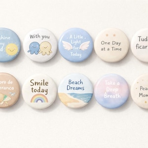 Può includere: Una collezione di dieci bottoni rotondi dai colori pastello con frasi e illustrazioni ispiratrici. I bottoni presentano frasi come "Sunshine on my mind", "Smile today" e "Beach Dreams", insieme a grafiche carine.