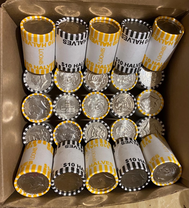 May include: A cardboard box filled with rolls of $10 half dollars. The rolls are white with yellow and black stripes and the text "LOOMIS" and "$10 HALVES". The coins are silver and feature a profile of a person.