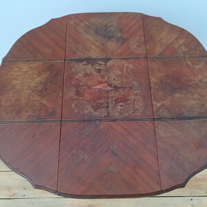 May include: A round, wooden table with a dark brown finish. The table has a scalloped edge and is composed of several rectangular panels. The wood grain pattern is visible throughout the table's surface.