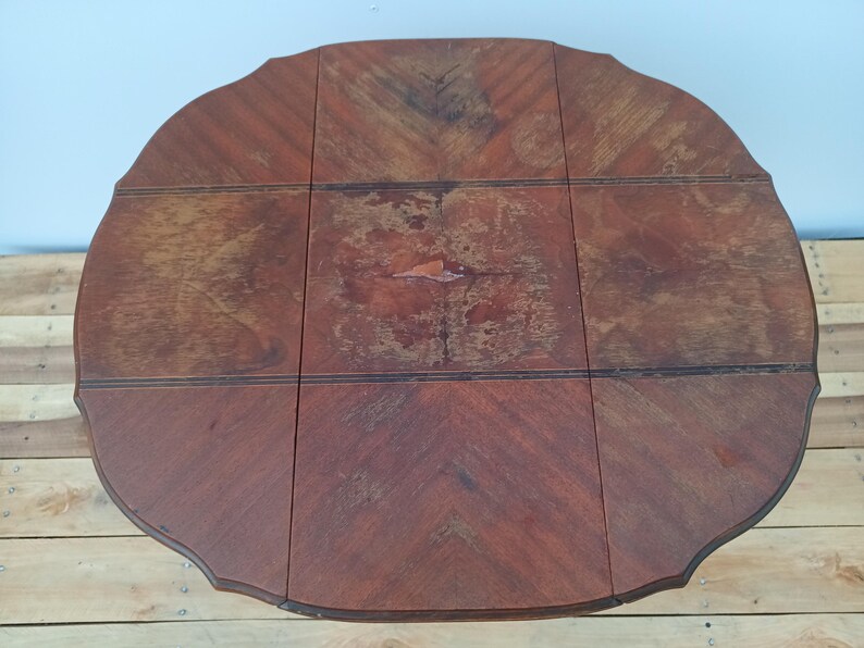 May include: A round, wooden table with a dark brown finish. The table has a scalloped edge and is composed of several rectangular panels. The wood grain pattern is visible throughout the table's surface.