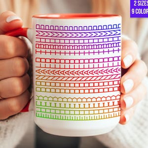 Könnte beinhalten: Weißer Keramikbecher mit rotem Innenraum und Griff, mit einem farbenfrohen geometrischen Muster. Der Becher hat den Text "2 SIZES 9 COLORS" in einem lila Feld.