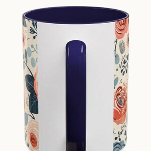 May include: White ceramic mug with a navy blue interior and handle. The mug features a floral design with red and peach roses, blue accents, and green leaves. The text "DESIGN DOES NOT CONTINUE UNDER THE HANDLE" is printed at the top.