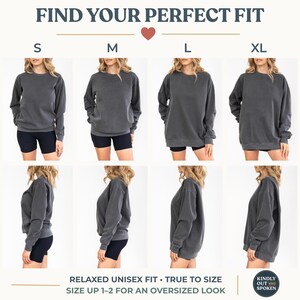 Op de afbeelding: Een antracietgrijs sweatshirt wordt getoond in de maten S, M, L en XL, met de tekst "FIND YOUR PERFECT FIT". Het sweatshirt wordt gecombineerd met een zwarte short. De tekst "RELAXED UNISEX FIT &bull; TRUE TO SIZE" is ook zichtbaar.