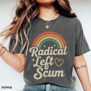Könnte beinhalten: Dunkelgraues T-Shirt mit Regenbogen-Design und dem Schriftzug "Radical Left Scum". Der Text ist in einer Retro-Schriftart mit einem Herzsymbol gehalten. Das Shirt hat einen Vintage-Look.