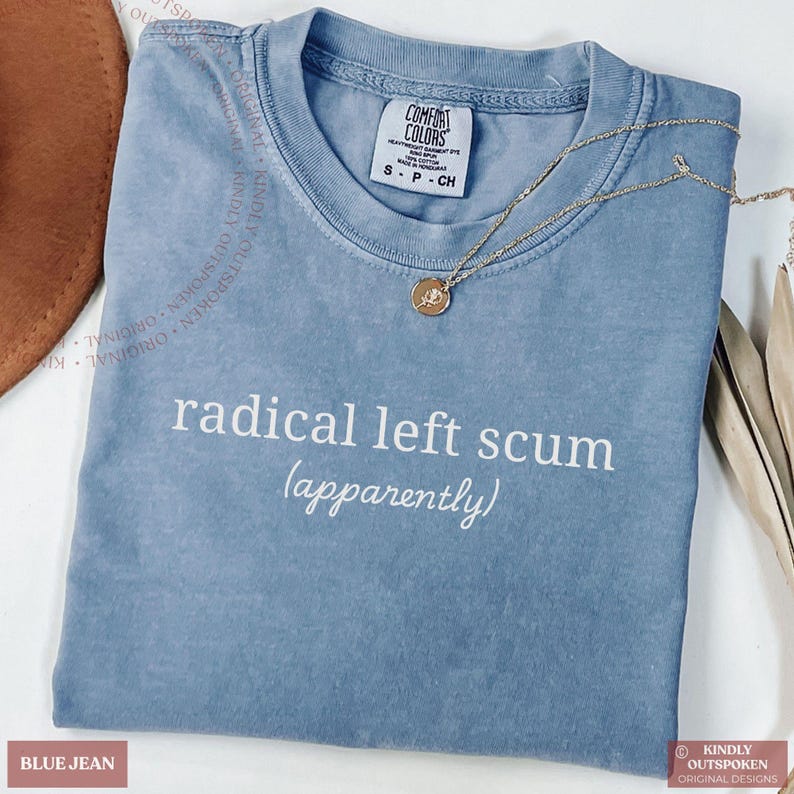 May include: A blue jean colored t-shirt with the white text "radical left scum (apparently)" printed on the front. The shirt features a Comfort Colors brand label at the neckline and is displayed with a gold-toned pendant necklace.